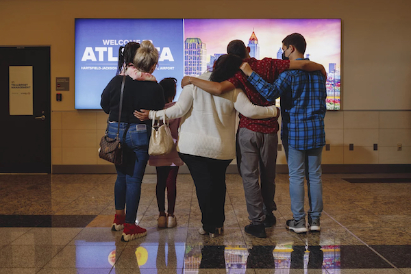 With, backs turned to the viewer, Ms. AB hugging family in front of a sign that says Welcome to Atlanta in the airport.