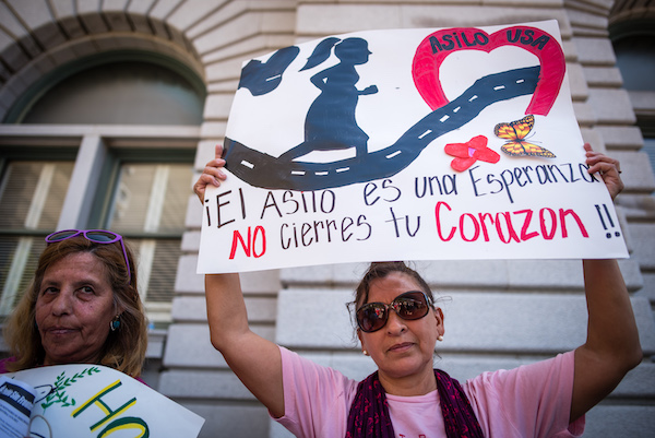 Protester holding up sign that says "¡El asilo es una esperanza; no cierres tu corazon! (Translation: Asylum is a hope; don't close your heart.)