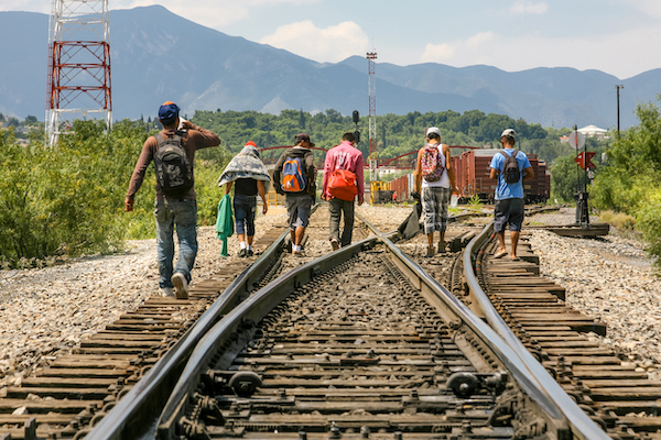 A group of Central American migrant walking along railroad tracks.