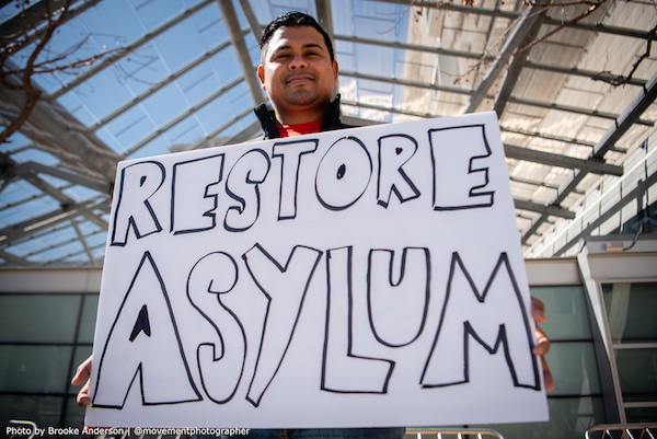 Man holding protest sign that says Restore Asylum.